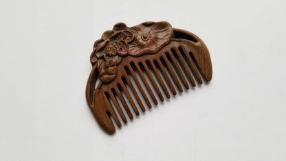 A brown sandalwood comb with a carved lotus design. The comb has a curved shape and a row of evenly spaced teeth. pocket size and eco-friendly