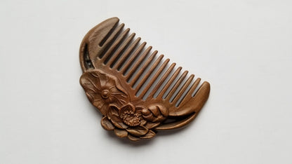 A brown wooden comb with a carved lotus design. The comb has a half-circle shape and is made of sandalwood, aromatic, anti static, sustainable beauty