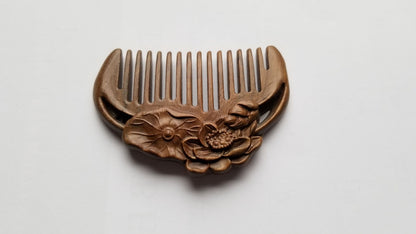A mini hand carved sandalwood comb with a lotus design. It has a row of evenly spaced teeth. plastic free wood comb, zero waste beauty and travel size, comes with a fabric gift bag. 