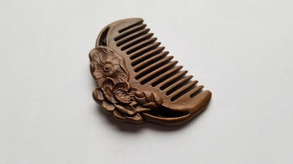 A mini sandalwood comb has a curved shape and is carved with two lotus flowers.  Natural hair care accessory and natural beauty.  Sustainable gift and comes with a fabric gift bag