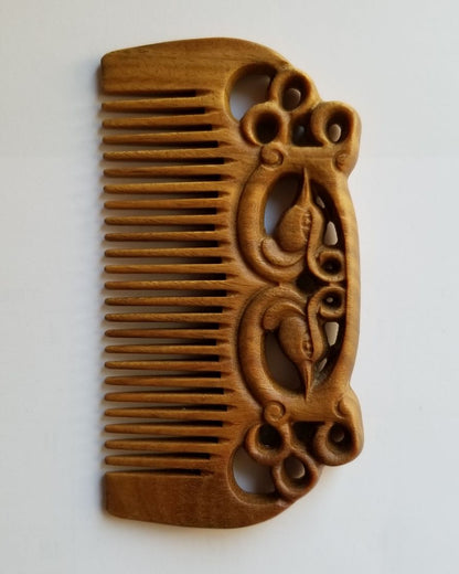 East Asian Phoenix Sandalwood Comb flat lay — front view showing symmetrical hand-carved phoenix pattern and fine teeth on green sandalwood