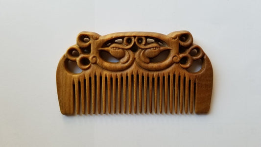East Asian Phoenix Sandalwood Comb flat lay — front view showing symmetrical hand-carved phoenix pattern and fine teeth on green sandalwood