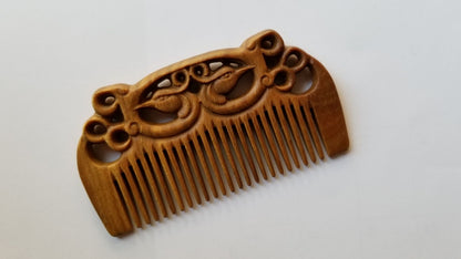 East Asian Phoenix Sandalwood Comb flat lay — three-quarter view showing symmetrical phoenix carving and natural sandalwood grain