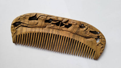 Wooden comb with intricate carvings of birds and foliage. The comb is made of light brown wood and features fine teeth for grooming. The detailed carving adds a decorative element to the functional hair care item.