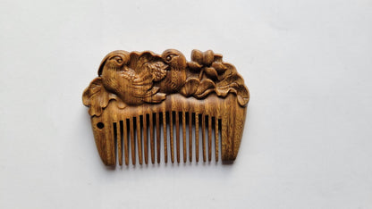 Mandarin duck hand carved wood comb with fine teeth facing up, natural green sandalwood grain visible