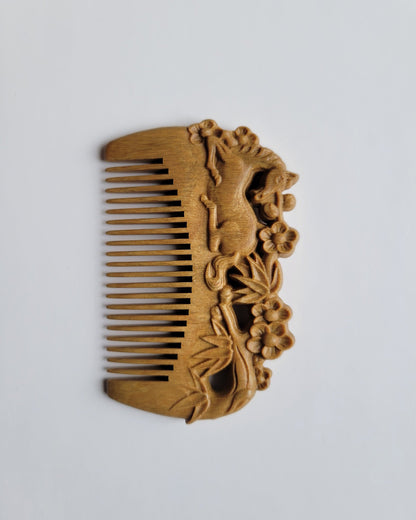 A small hand carved wood comb with horse, bamboo, plum blossom design. it has rounded smooth fine teeth. 