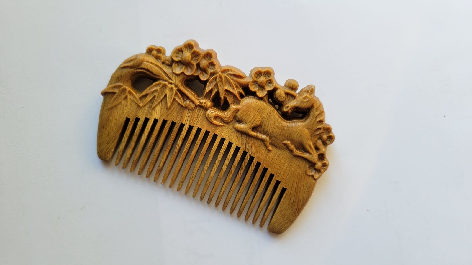 A pocket size  wooden comb with a delicate carving. This carving in this comb includes a laying horse, bamboo, and plum blossom. It is inspired by the poem “Parting at Changgan," written by famous Chinese poet Li Bai. 