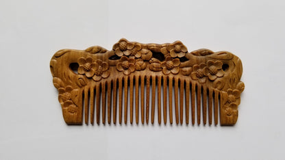 Handcrafted Wooden comb with intricate floral carvings. The comb features a series of fine teeth and a decorative top adorned with carved plum blossom. The wood has a warm, natural tone. 