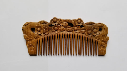 Handcrafted Wooden comb with intricate floral carvings. The comb features a series of fine teeth and a decorative top adorned with carved plum blossom. The wood has a warm, natural tone. 