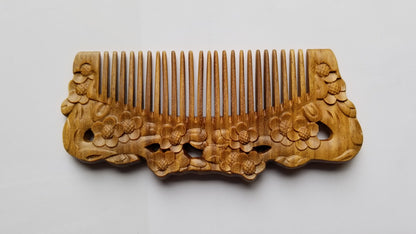 Wooden comb with intricate floral carvings. The comb is made of light brown wood and features detailed carvings of flowers along the handle. The teeth of the comb are evenly spaced. The comb is a hair care accessory. best birthday gift for her