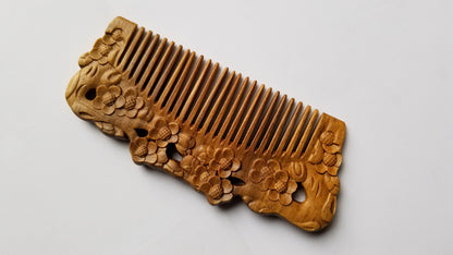 A sandalwood comb with intricate floral carvings and features detailed carvings of plum blossom along the top edge. The teeth of the comb are evenly spaced. Vintage style wood comb and great for birthday gift