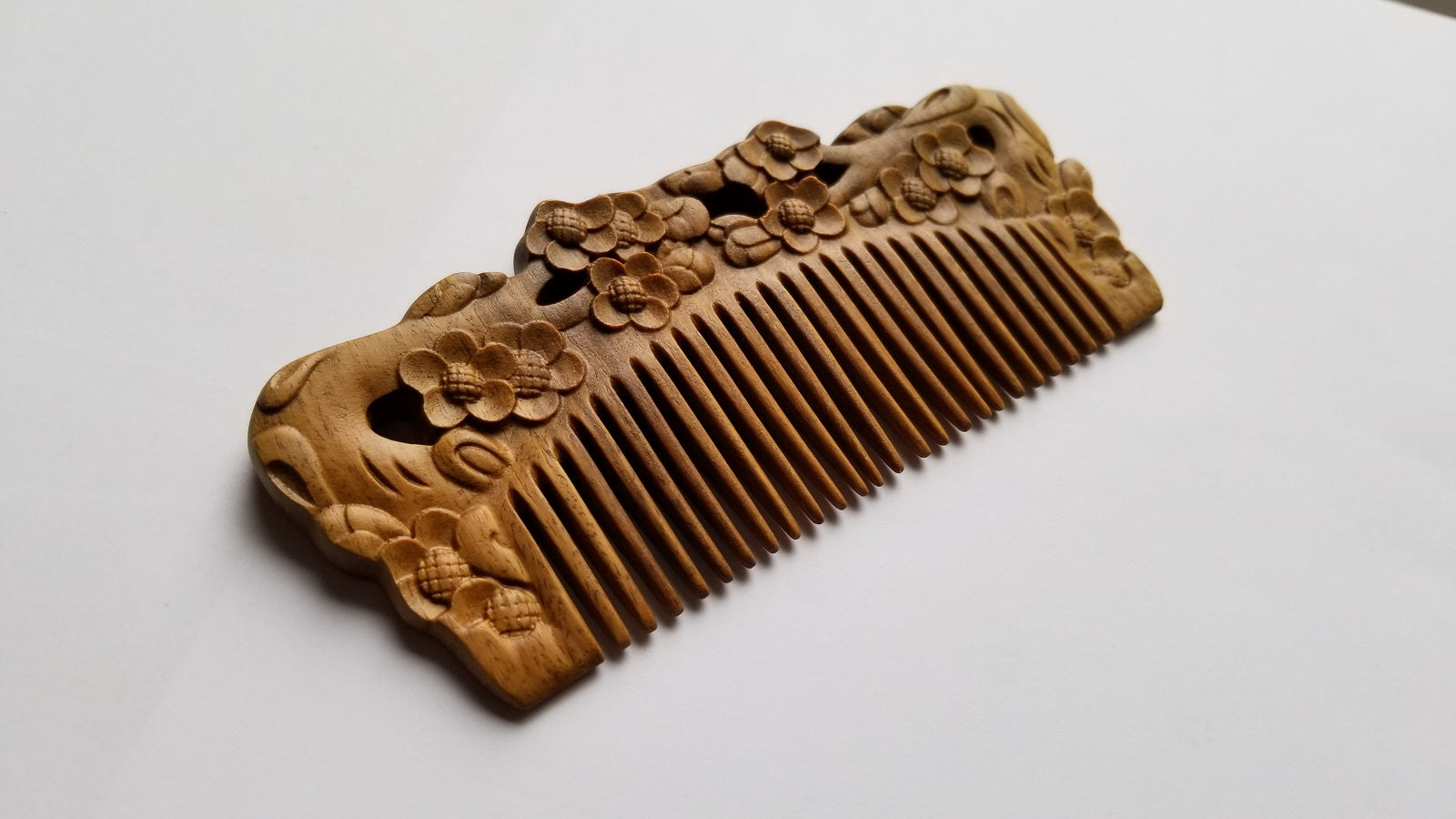 Wooden comb with intricate floral carvings. The comb features a series of evenly spaced teeth and is adorned with detailed plum blossom designs along the handle. The wood has a natural, light brown color.