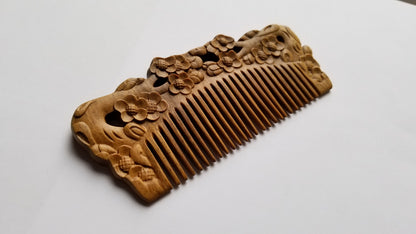 Wooden comb with intricate floral carvings. The comb features a series of evenly spaced teeth and is adorned with detailed plum blossom designs along the handle. The wood has a natural, light brown color.