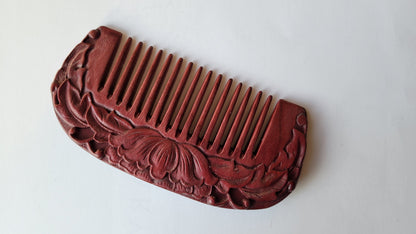 A purple heart wood comb with a carved lotus motif on one side the the comb. The comb has fine teeth. It comes with a fabric gift bag.
