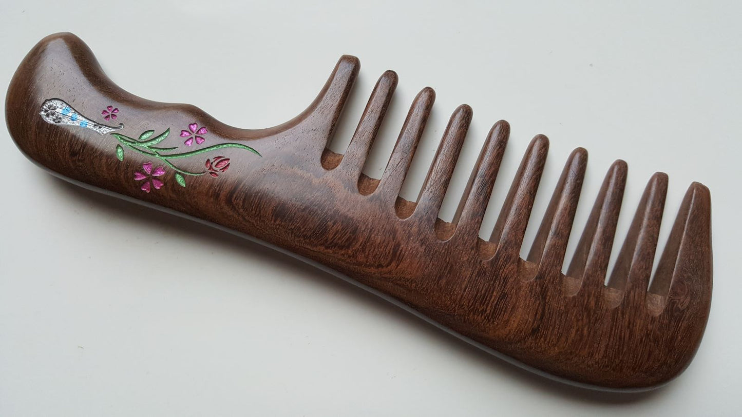 A dark brown wooden comb with a floral vase design on the handle. The flowers are pink and green in a silver-colored vase. Gift for Women