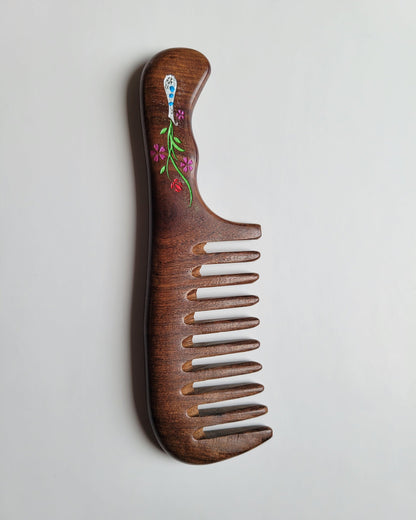 A brown Sucupira wood comb with a floral design slightly carved into the handle. The flowers are pink, green, and white. This wood comb has extra wide teeth and is good for curly, long, and thick hair. Gift for mom
