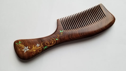 A brown wooden comb with a floral design carved into the handle. The design features a ivy and flower in a gold, white, and green color.