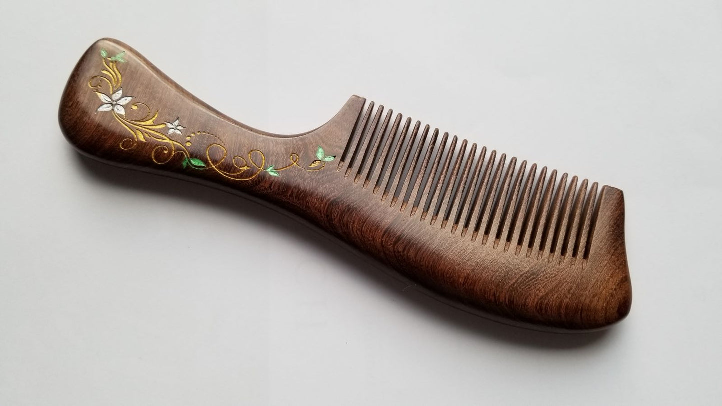 A brown wooden comb with a decorative ivy design on the handle. The comb has a curved shape and is made of natural Sucupira wood.