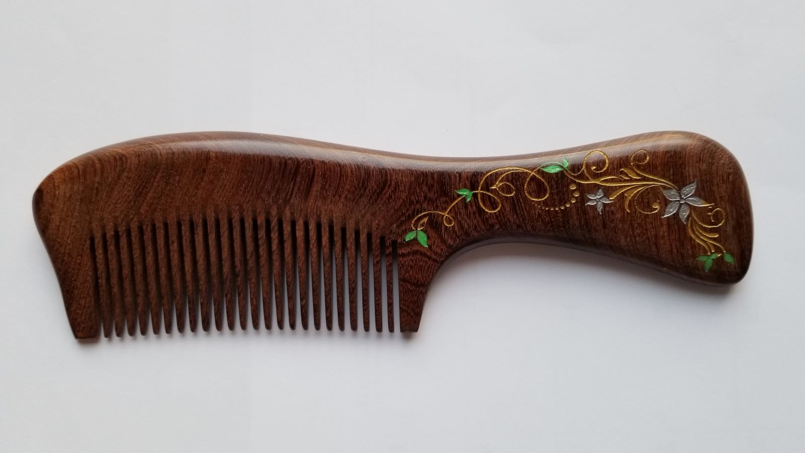 A dark brown wooden comb with a decorative floral design on the handle. The design features elegant ivy in gold, white and green. Great gift for her