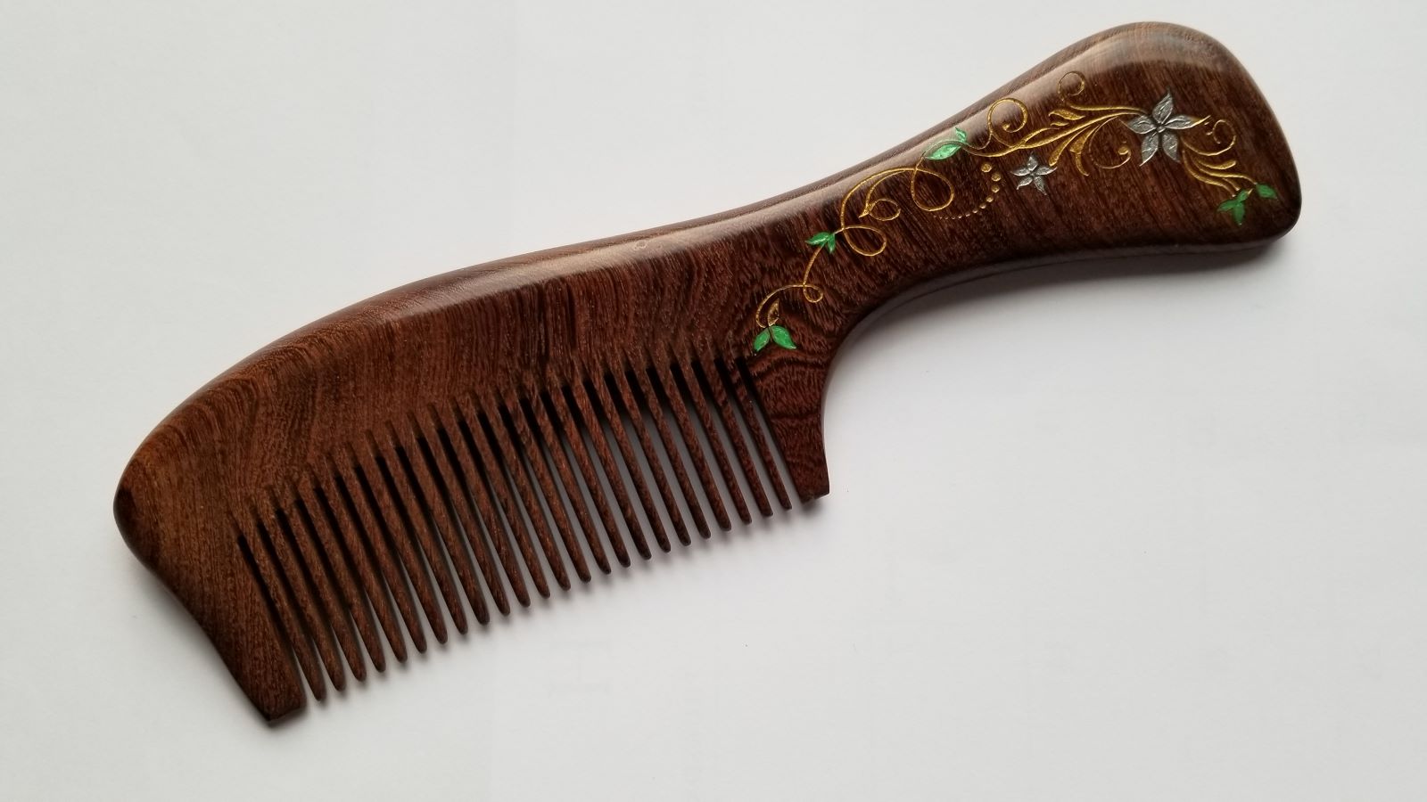 A brown wooden comb with a floral design on the handle. The design is in gold, white and green. and features ivy and vines. It includes fine teeth for fixing hair.