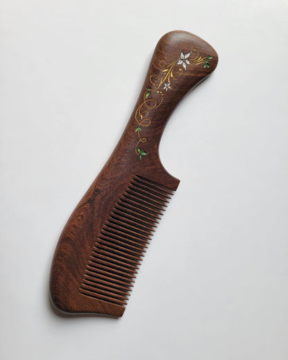 A dark brown Sucupira wood comb with an intricate floral design on the handle. This comb is designed for all hair. Great mother's day gift with gift bag