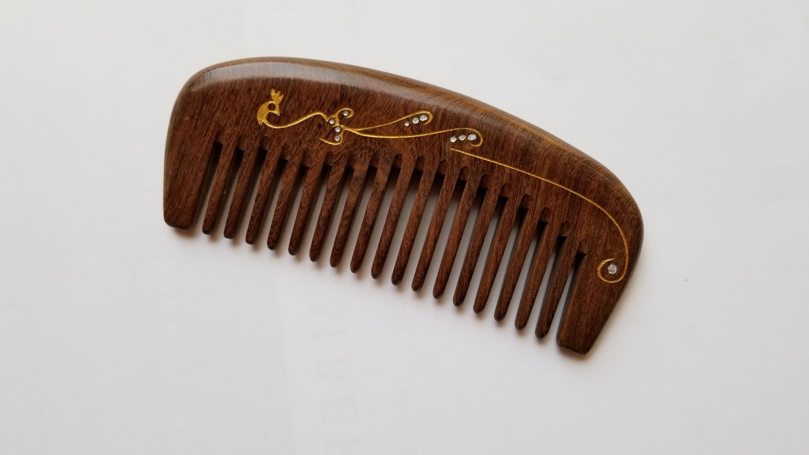 A wooden comb with a dark brown finish and a decorative gold design. The comb has evenly spaced teeth and a curved shape. The gold design features a flowing pattern with small, abstract accents.