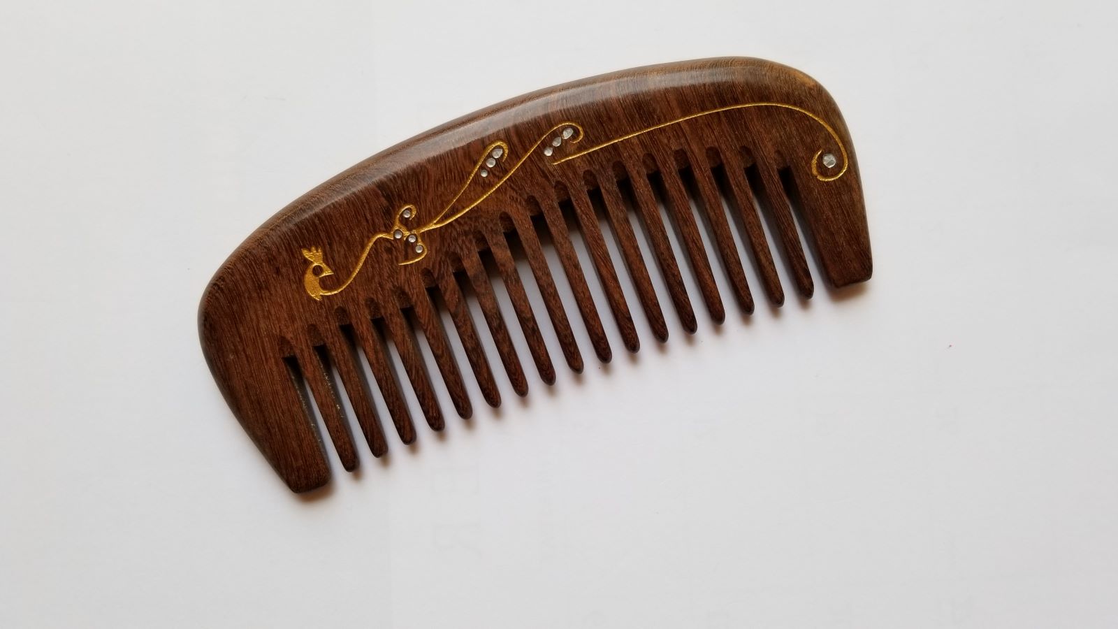 Close-up of gold peacock design with flowing pattern and abstract accents on wood comb handle — Arakicrafts. The design curves along the edge and across the comb's surface, adding an elegant touch.