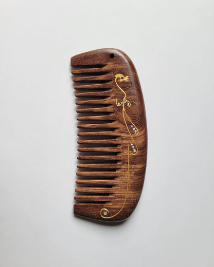 Close-up of gold peacock design with flowing pattern and abstract accents on wood comb handle — Arakicrafts. The design curves along the edge and across the comb's surface, adding an elegant touch.