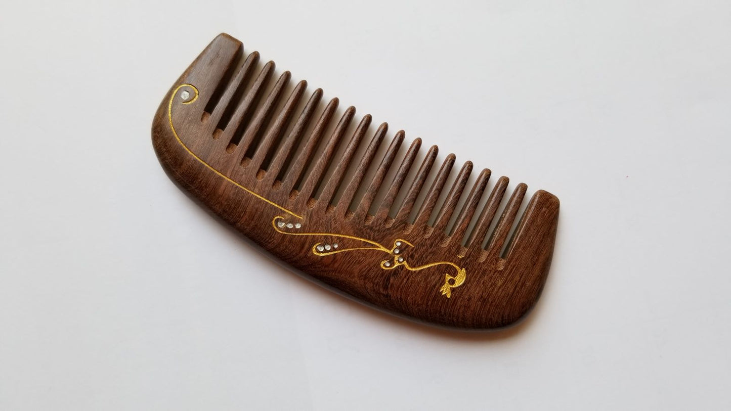 Handcrafted wood comb with gold peacock motif, flat lay angled view of single-piece hardwood construction — Arakicrafts. The comb has closely spaced teeth and is designed for hair grooming.