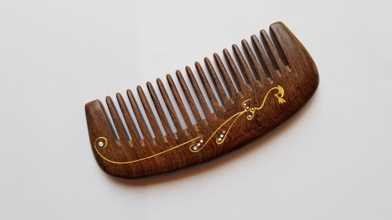 Wide tooth anti-static wood comb for curly, thick, and wavy hair, flat lay overhead view — Arakicrafts.  The design is on the handle and along the side.