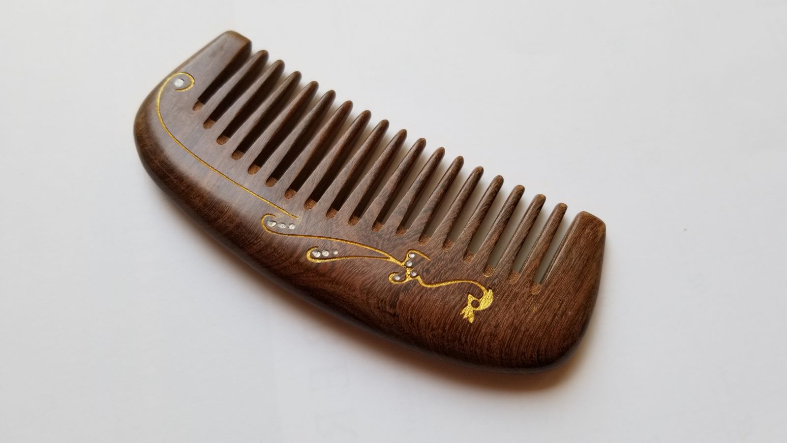 Natural hardwood comb for women — gold peacock design on dark brown Sucupira wood — Arakicrafts. The comb has a curved handle and evenly spaced teeth, suitable for hair grooming.