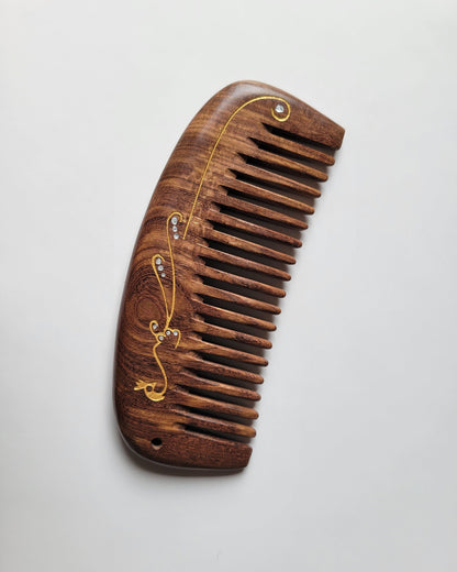 Natural hardwood comb for women — gold peacock design on dark brown Sucupira wood — Arakicrafts. The comb has a curved handle and evenly spaced teeth, suitable for hair grooming.