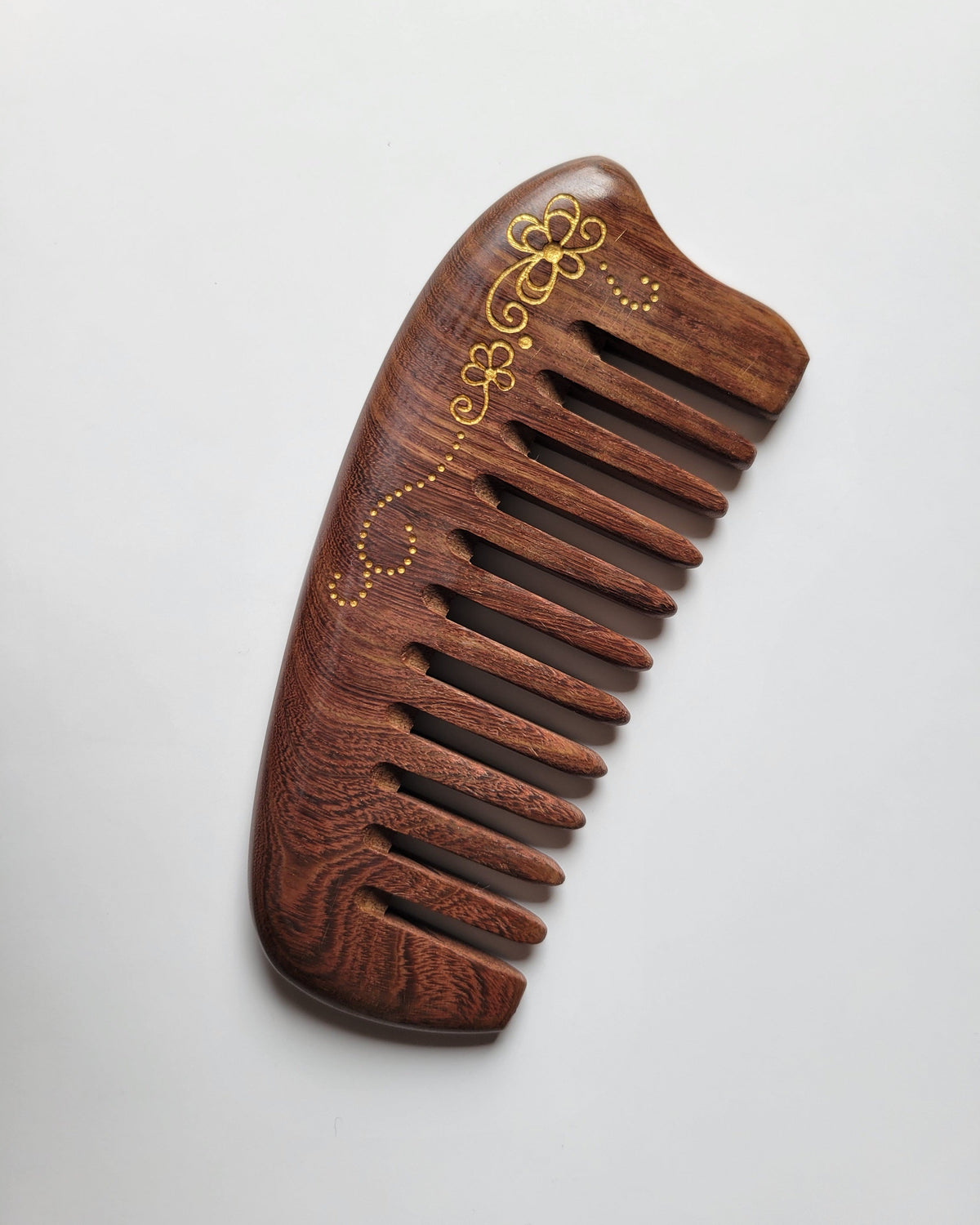 Wide tooth Sucupira wood comb overhead view, gold floral scroll detail, pocket-sized natural hardwood comb for thick and long hair