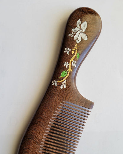 Hand painted magnolia flower wood comb in Sucupira hardwood, flat lay front view — Arakicrafts.  The design features white flowers, green leaves, and gold accents.