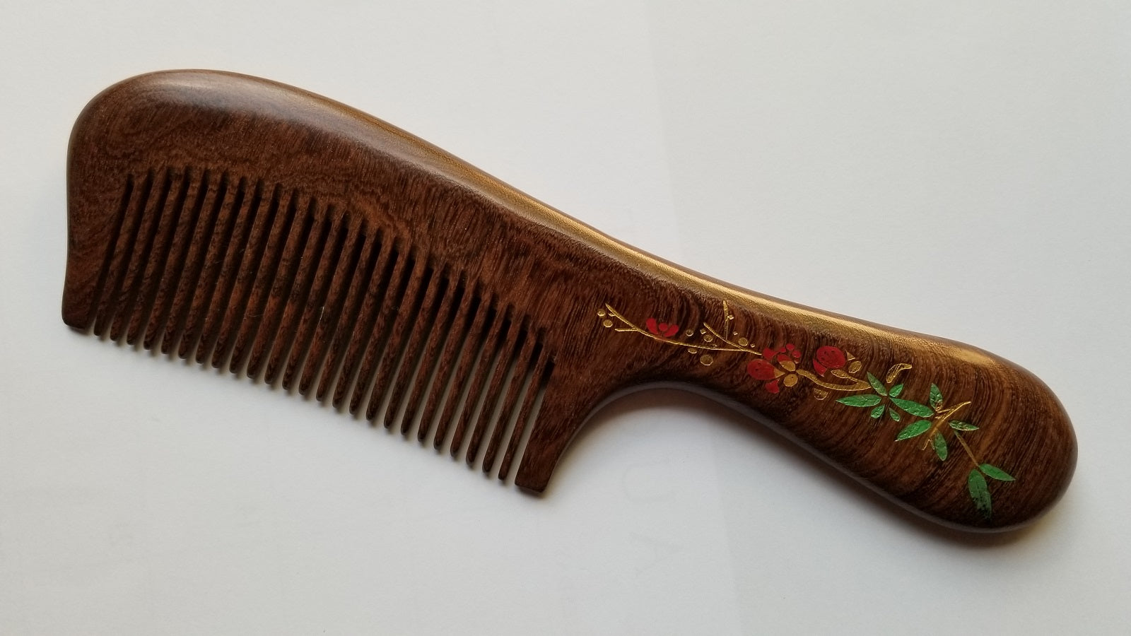 A brown wooden comb with a red plum blossom design painted on the handle. The comb has a curved shape and a long handle.