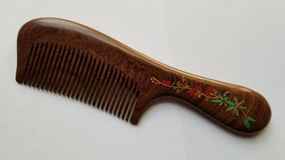A brown wooden comb with a red plum blossom design painted on the handle. The comb has a curved shape and a long handle.