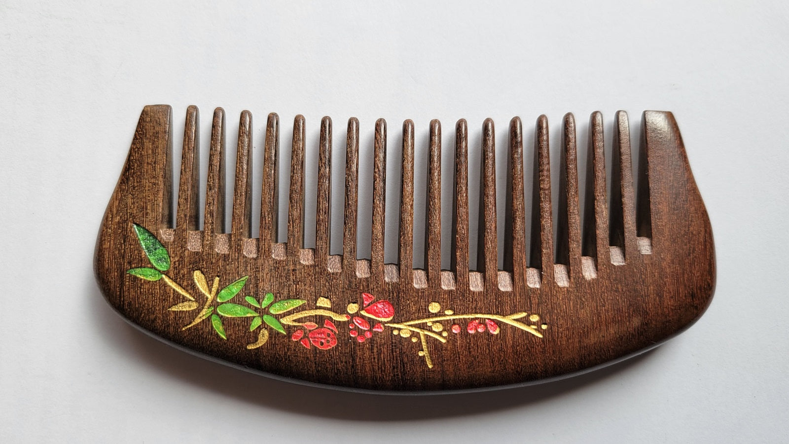 Dark brown Sucupira wood wide tooth pocket comb with curved handle, flat lay side angle — Arakicrafts