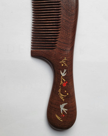  A wooden comb with a dark brown finish. The handle features an ornate design with silver swallow birds, red flowers, and gold accents. The comb's teeth are finely spaced, and the overall design is elegant.
