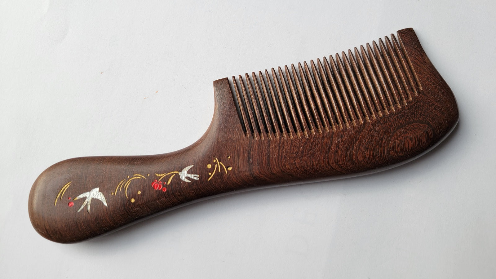 Dark brown Sucupira wood fine tooth comb with ornate painted handle, flat lay side angle — Arakicrafts