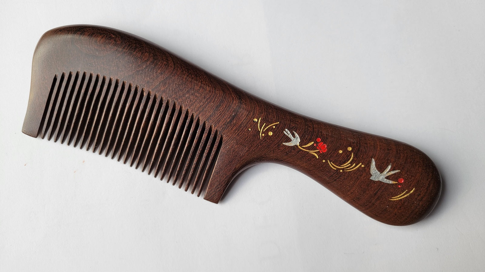 Handcrafted wood comb with swallow and floral motif, flat lay angled view showing single-piece hardwood grain — Arakicrafts