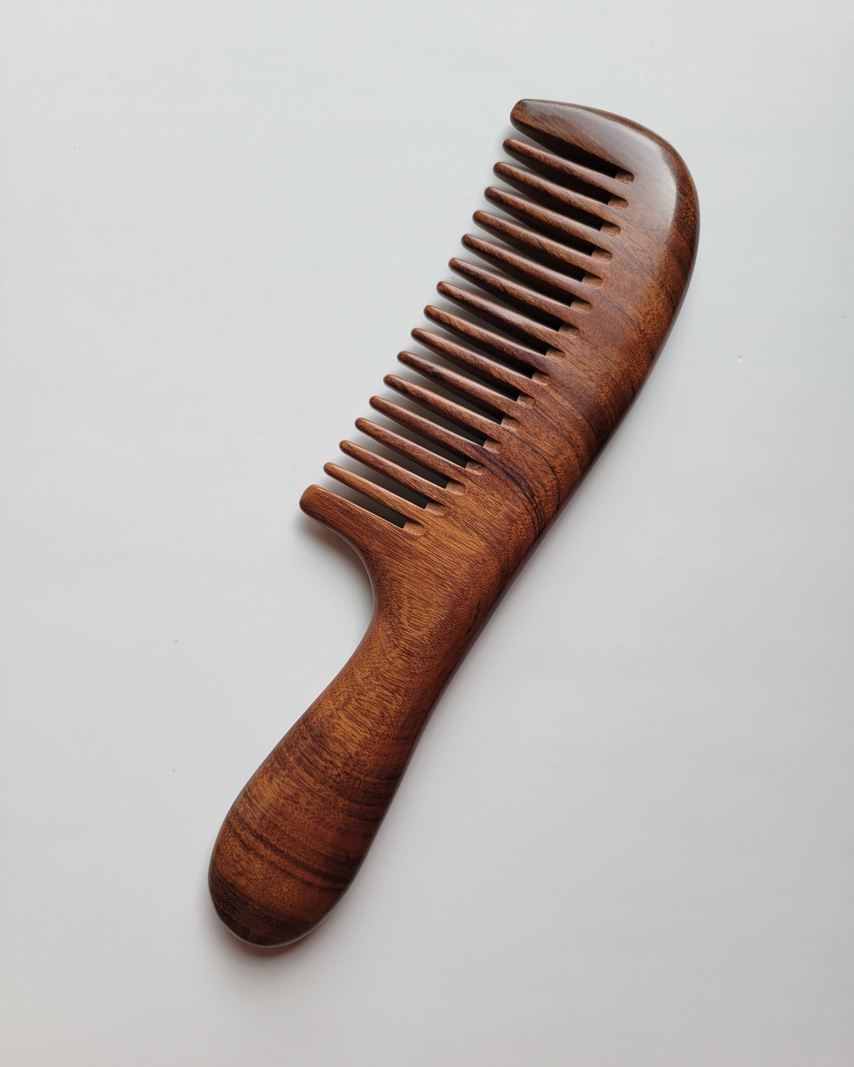 Wide tooth wood comb with curved handle, flat lay side angle showing smooth polished finish — Arakicrafts