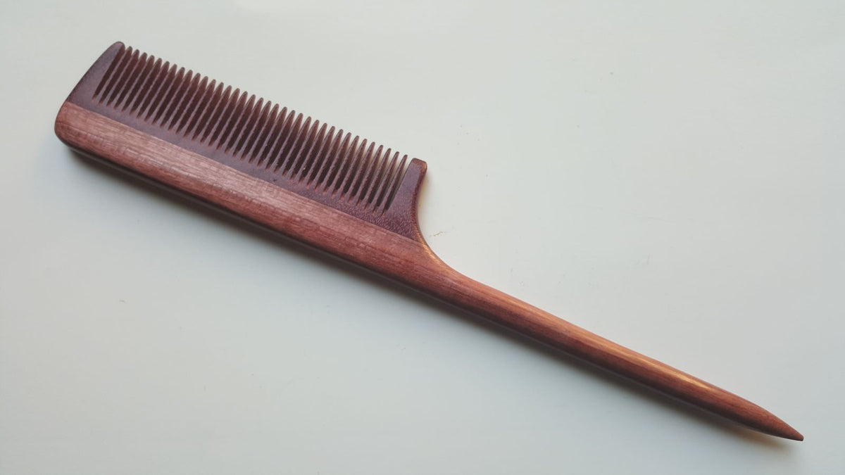 A long, wooden rat tail comb with a pink finish. The comb has a long, thin handle and a narrow, rectangular head with fine teeth.