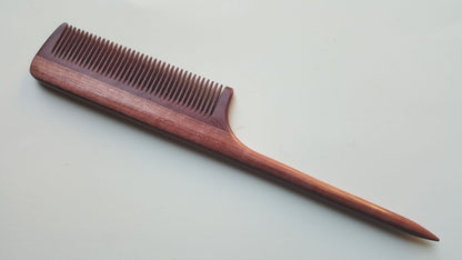 A long, wooden rat tail comb with a pink finish. The comb has a long, thin handle and a narrow, rectangular head with fine teeth.