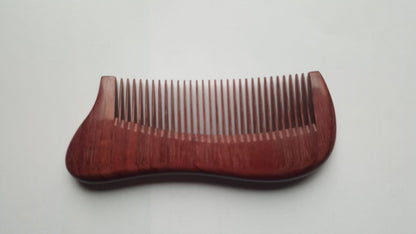 A wooden comb with a curved handle and fine teeth. The comb is made of a reddish-brown wood and has a smooth, polished finish. The teeth are evenly spaced and designed for grooming hair and beard.