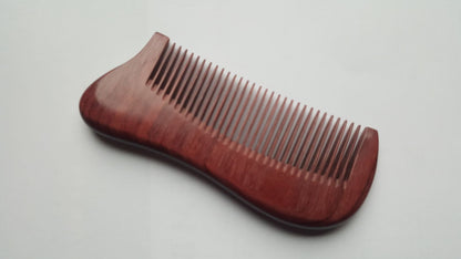 A purple heart wood comb with a dark reddish-brown finish. The comb has a curved handle and closely spaced teeth. The comb is approximately 4.9 inches long and is designed for hair grooming.
