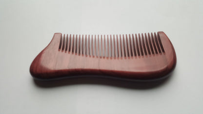 A wooden comb with a curved handle and fine teeth. The comb is made of a purple heart wood and has a smooth, polished finish. The comb is designed for grooming hair and beard. Great gift for him and comes with a gift bag. 