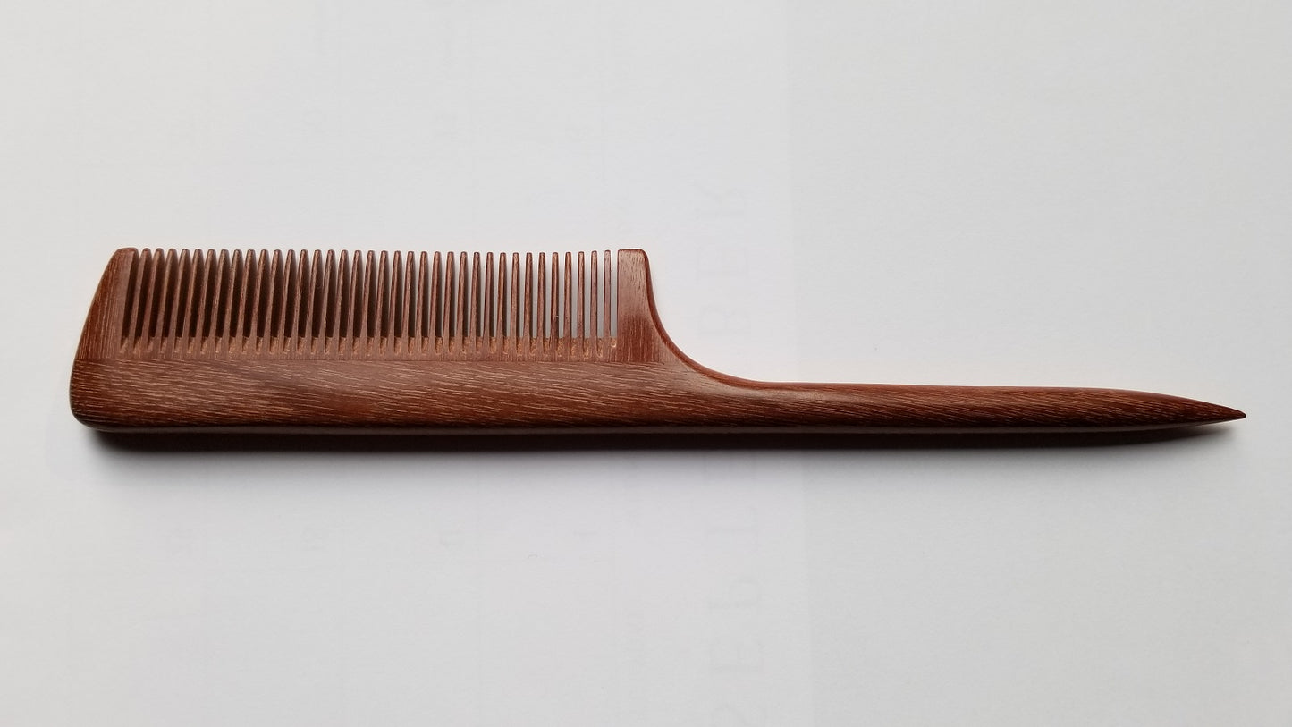 A brown wooden comb with a long, thin handle. The comb has a rounded edge and a pointed tip.