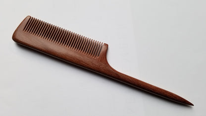 A long, wooden comb with a brown, reddish hue. The comb has a long, thin handle and  a slim, rectangular comb section. it's designed for hair styling and sectioning.