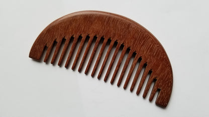 A wooden comb with a curved, half-moon shape. The comb is made of a dark brown wood and has evenly spaced teeth. The comb is designed for hair care and grooming.