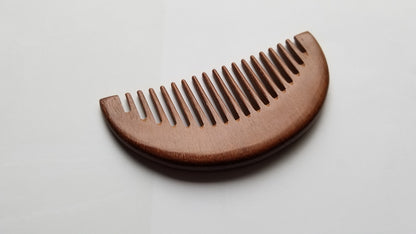 A wooden comb with a curved top and closely spaced teeth. The comb is made of a reddish-brown pao rosa wood, and the grain is visible. The comb is designed for grooming hair and is a natural alternative to plastic combs.  One of a kind piece and perfect holiday gifts!